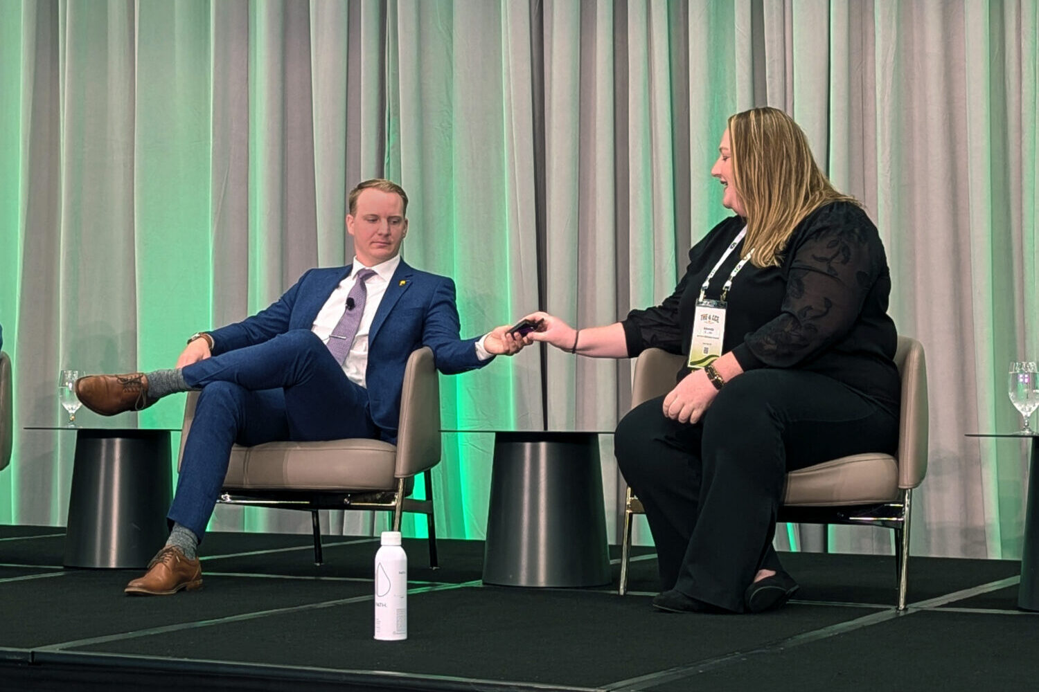Ben Rhodes of the Nebraska Ethanol Board, left, hands a microphone to Amanda Bechen of South Dakota Corn at the American Ethanol Coalition's annual conference on Aug. 22, 2025, in Sioux Falls. (John Hult/South Dakota Searchlight)