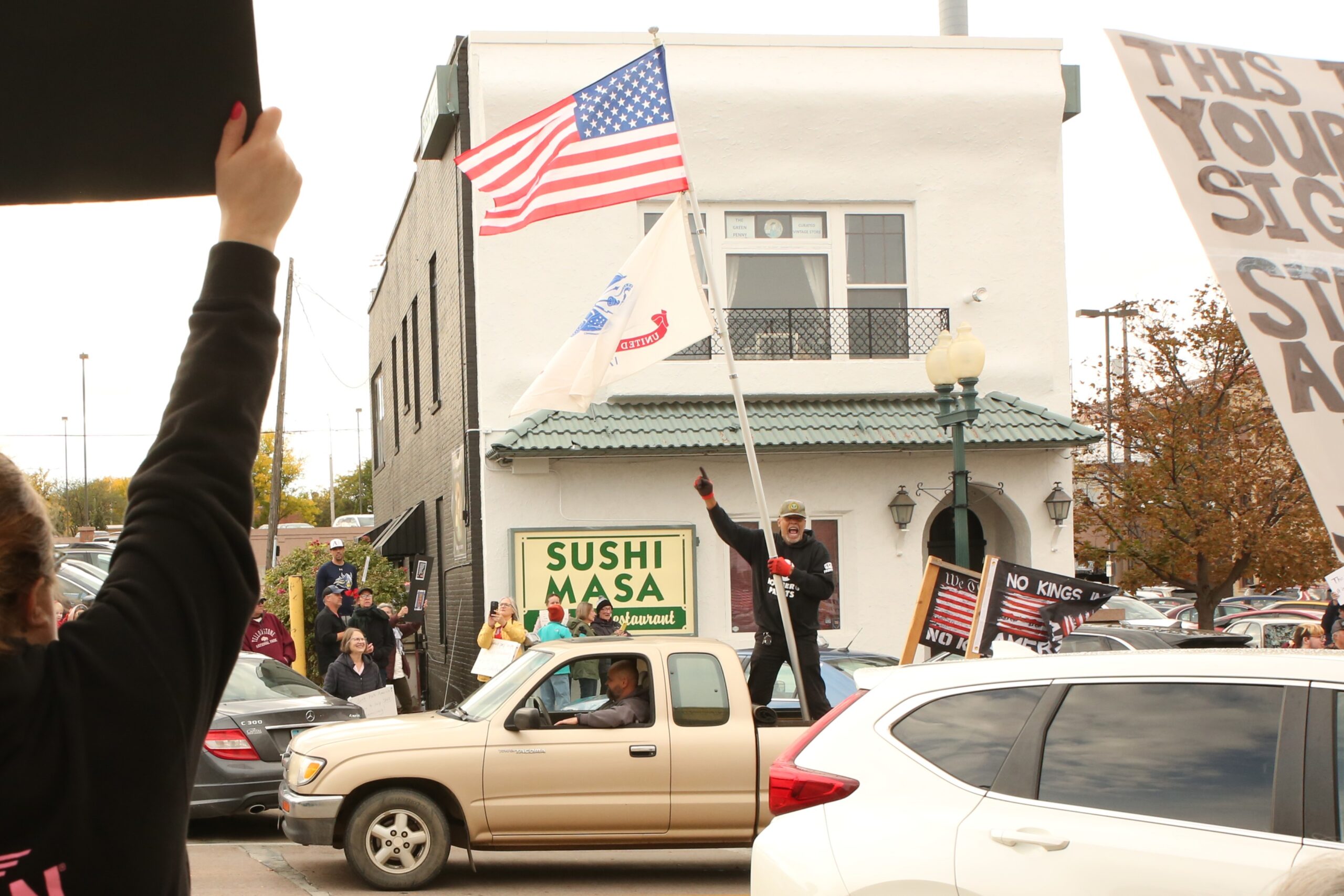 George Hamilton cheers on protesters while riding in the back of a pick up along Phillips Avenue in downtown Sioux Falls on Oct. 18, 2025 for the No Kings protest. (Photo by Makenzie Huber/South Dakota Searchlight)
