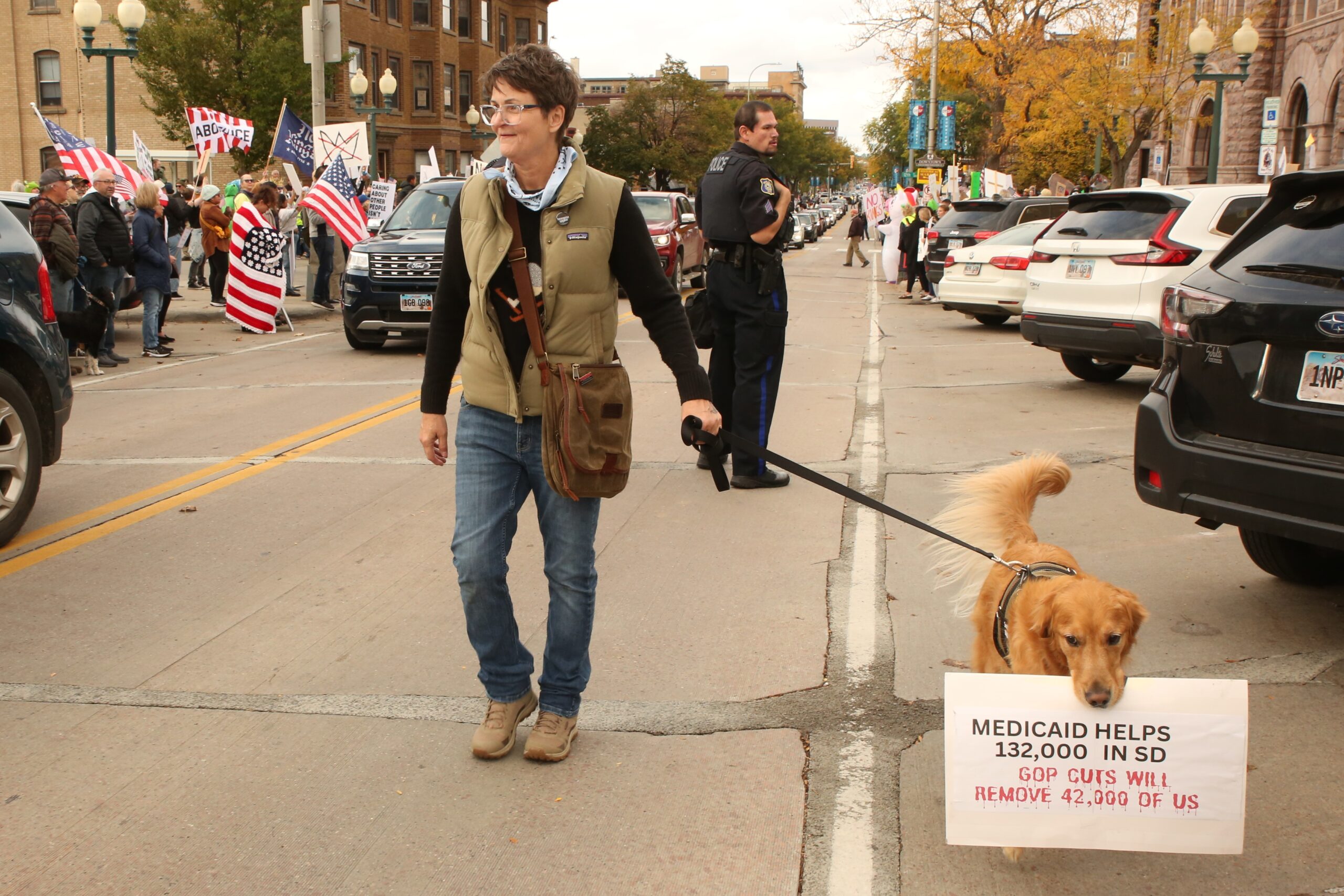 Nyna Nygaard walks her dog Henry along Phillips Avenue in downtown Sioux Falls on Oct. 18, 2025 for the No Kings protest. (Photo by Makenzie Huber/South Dakota Searchlight)