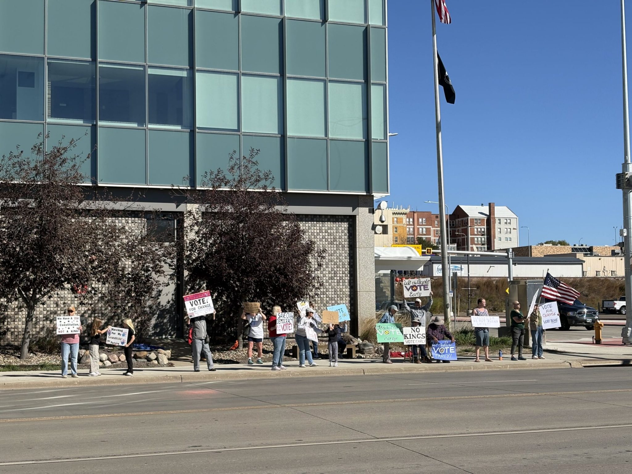 Demonstrators hold signs that encourage advance voting during a No Kings demonstration in Pierre, South Dakota, on Oct. 17, 2026. (Photo by Meghan O'Brien/South Dakota Searchlight)