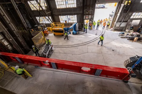 Technicians rig DUNE cryostat beams for loading into the cage--and begin lifting. 
