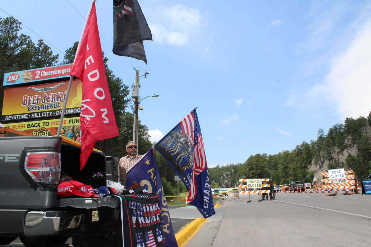 President Donald Trump supporter Rudy Martinez sets up flags and hats to sell along a highway on July 3, 2026, in Keystone, South Dakota. The highway leads to Mount Rushmore, where Trump was scheduled to speak before a fireworks display. (Photo by Joshua Haiar/South Dakota Searchlight)