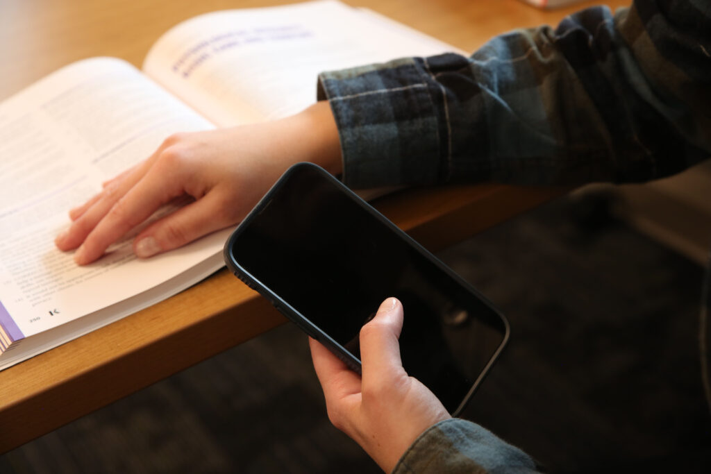 A person shields a cellphone with their arm while reading a book. (Photo illustration by Makenzie Huber/South Dakota Searchlight)
