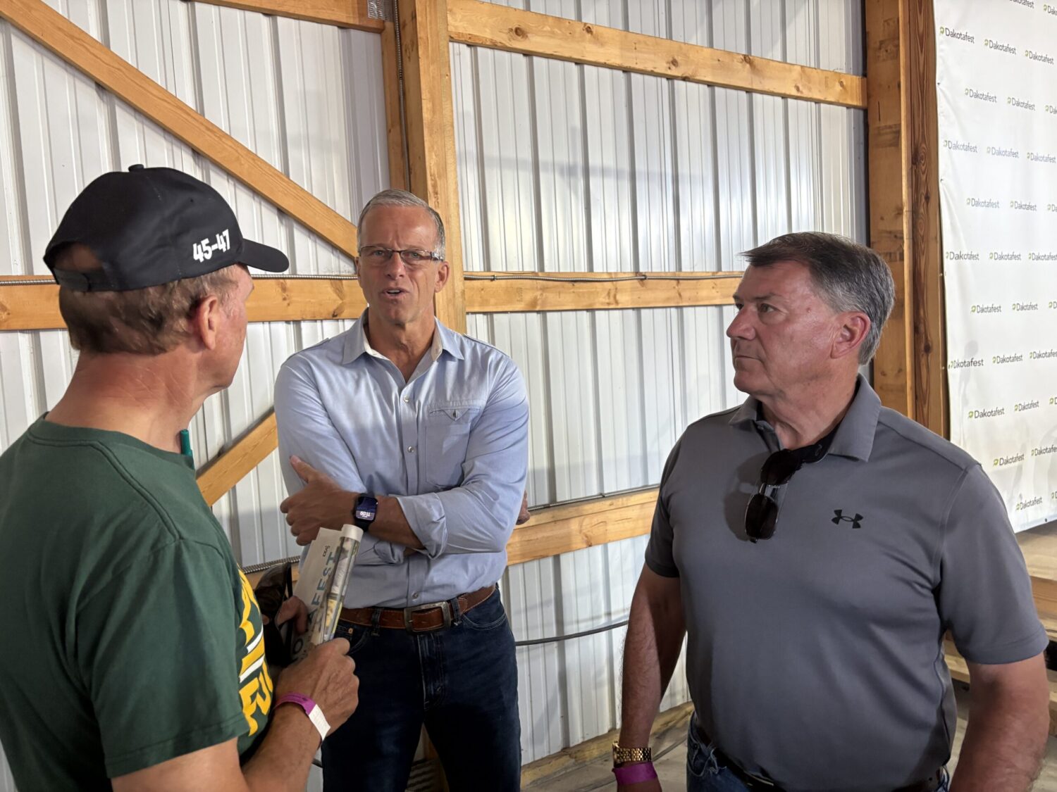 U.S. Senate Majority Leader John Thune and Sen. Mike Rounds, both Republicans from South Dakota, speak with an attendee of Dakotafest in Mitchell on Aug. 19, 2026. (Photo by Joshua Haiar/South Dakota Searchlight)
