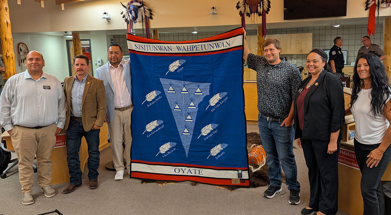 From left, Rep. Eric Emery, D-Rosebud, Rep. Will Mortenson, R-Pierre, Sisseton-Wahpeton Oyate Tribal Chairman J. Garret Renville, Sen. Mike Rohl, R-Aberdeen, Sen. Tamara Grove, R-Lower Brule, and Rep. Heather Baxter, R-Rapid City, pose for a photo with a pendleton blanket given to lawmakers on the State-Tribal Relations Committee by the tribe. (John Hult/South Dakota Searchlight)