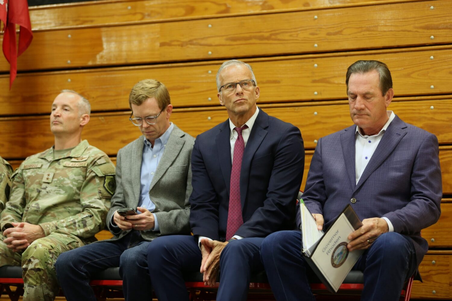 From left: Adjutant General Mark Morrell, U.S. Rep. Dusty Johnson, U.S. Sen. John Thune, and Gov. Larry Rhoden, wait for the start of a ceremony in Wagner, South Dakota, on Oct. 22, 2026, honoring about 120 South Dakota National Guard soldiers preparing to deploy to the U.S.-Mexico border for a year. (Photo by Joshua Haiar/South Dakota Searchlight)