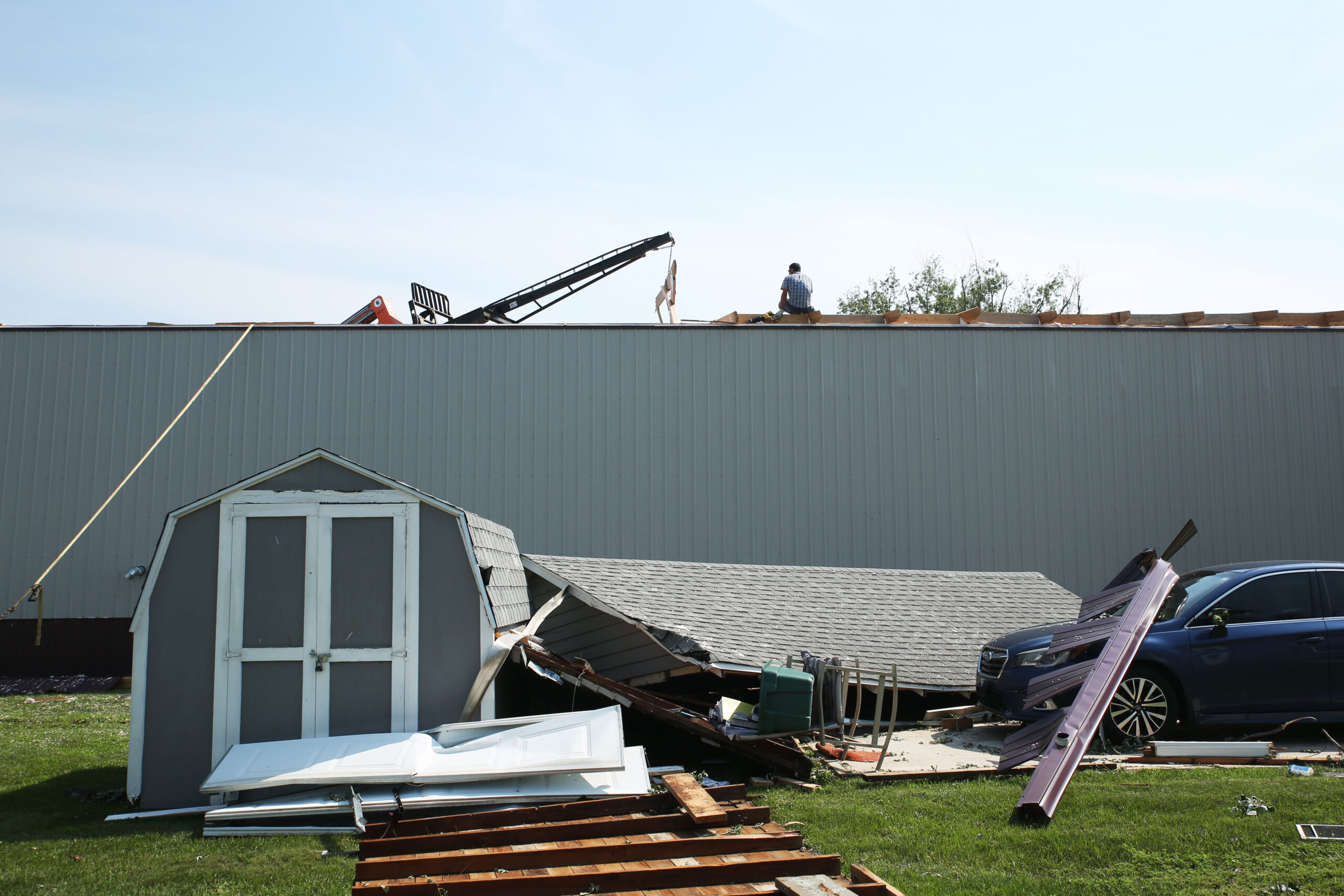 A clean-up volunteer sits on top of a damaged warehouse roof in Hudson on Tuesday, July 29, 2025 after severe weather moved through the area Monday evening damaging trees, homes and other structures. (Makenzie Huber/South Dakota Searchlight)