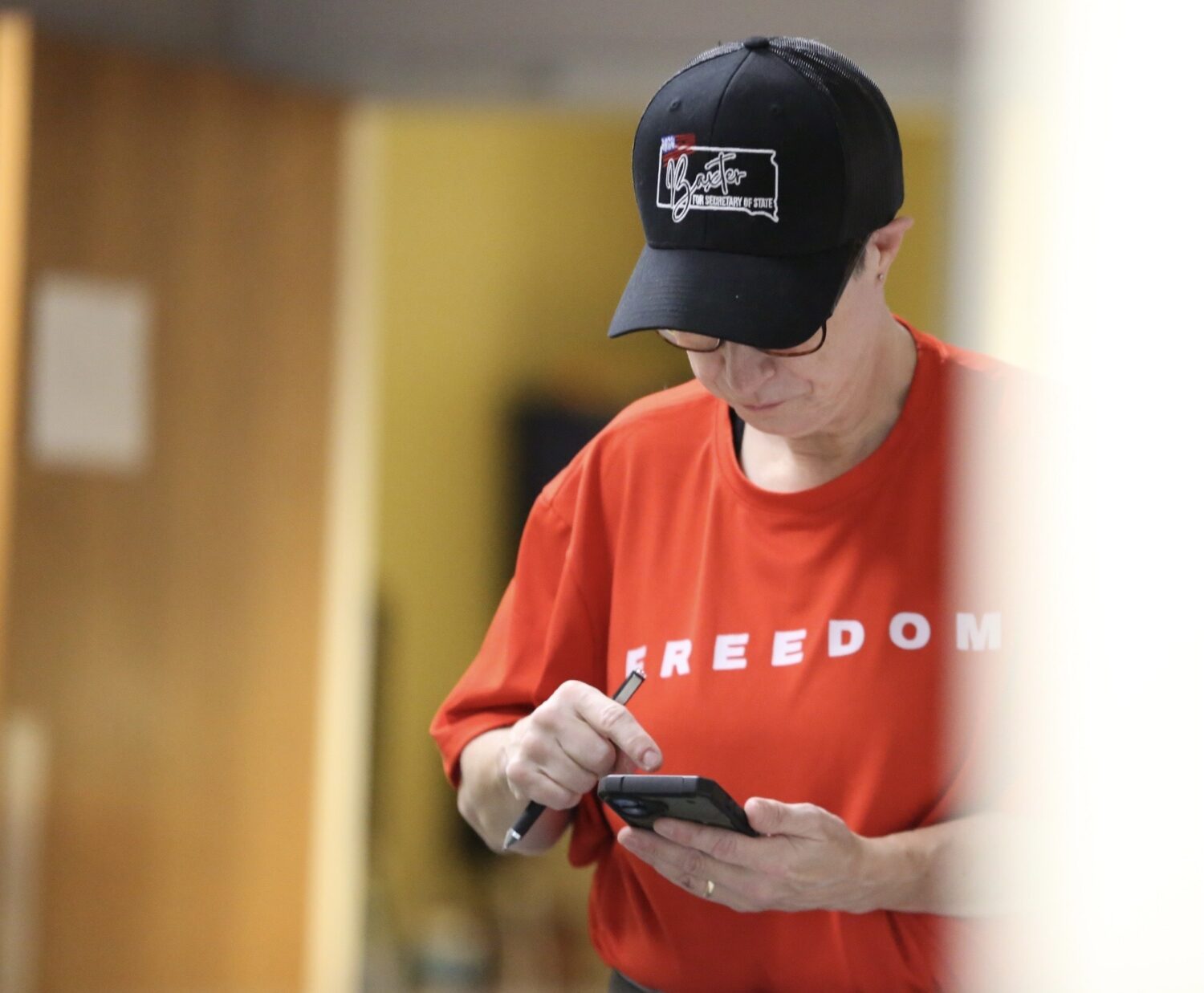 Gretchen Weible wears a Heather Baxter for secretary of state hat and checks her phone during an election hand count demo in Sioux Falls on Nov. 14, 2025. (Photo by Joshua Haiar/South Dakota Searchlight)